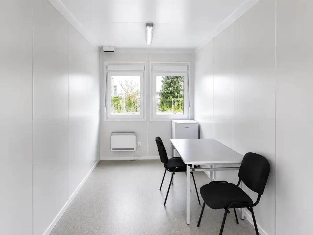 Moderner Bürocontainer von Spacetainer mit Schreibtisch, zwei Stühlen und Kühlschrank.